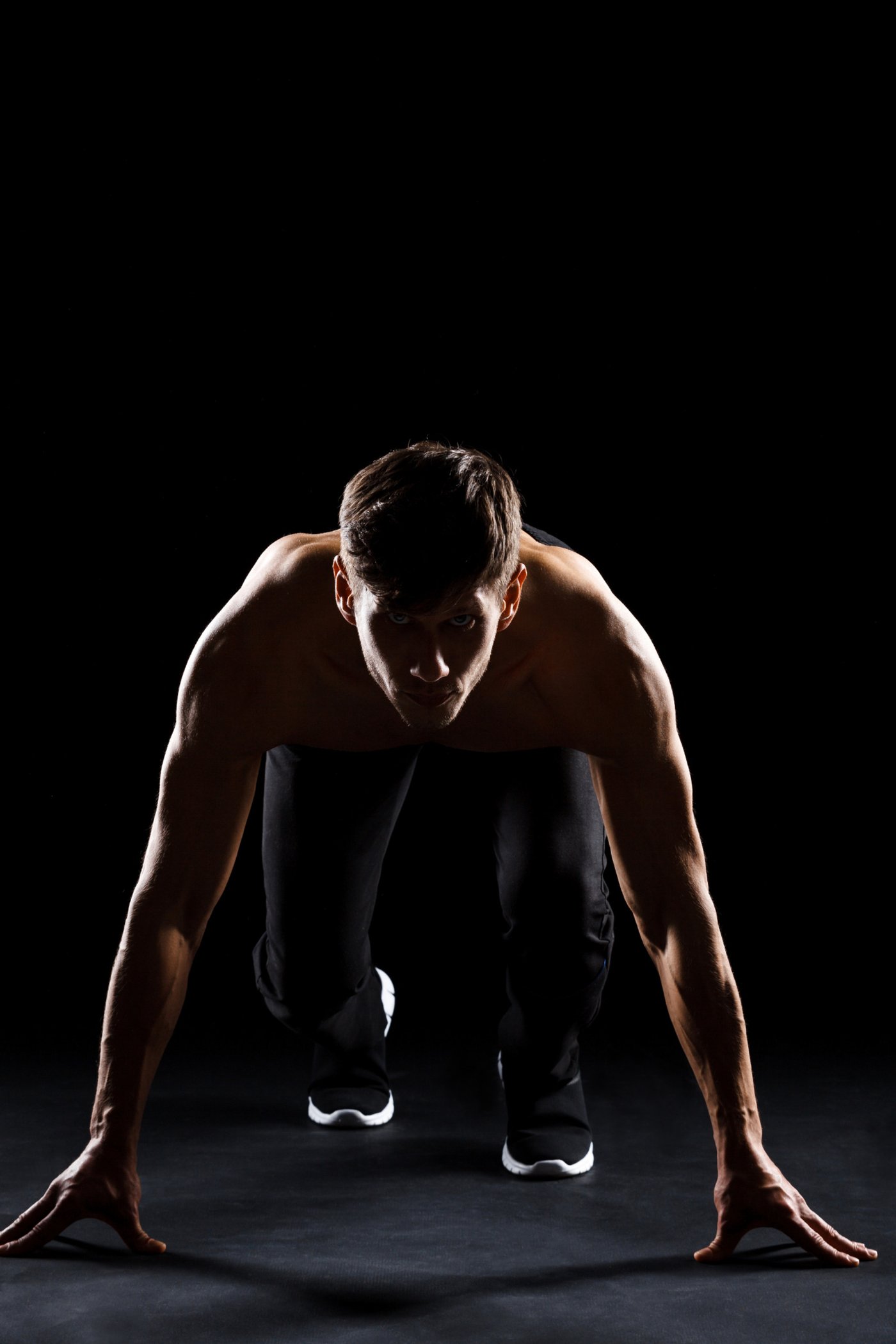 Atleta pronto allo scatto in posizione di partenza, illuminazione drammatica su sfondo scuro
